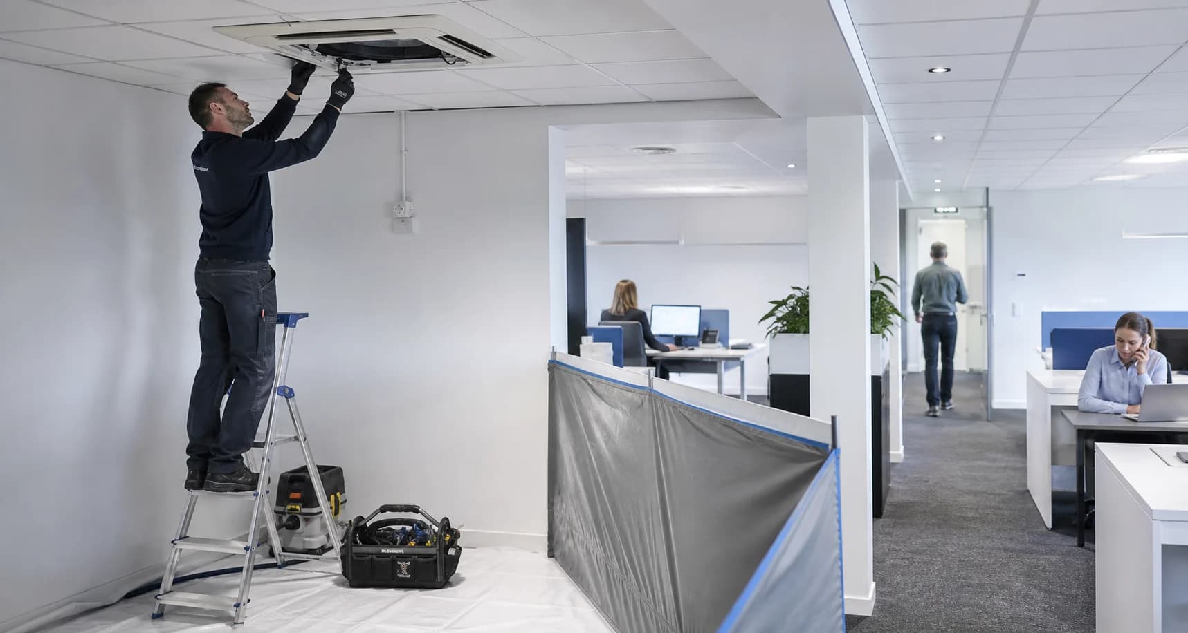 Monteur werkt in een afgeschermde zone terwijl medewerkers in het kantoor doorwerken