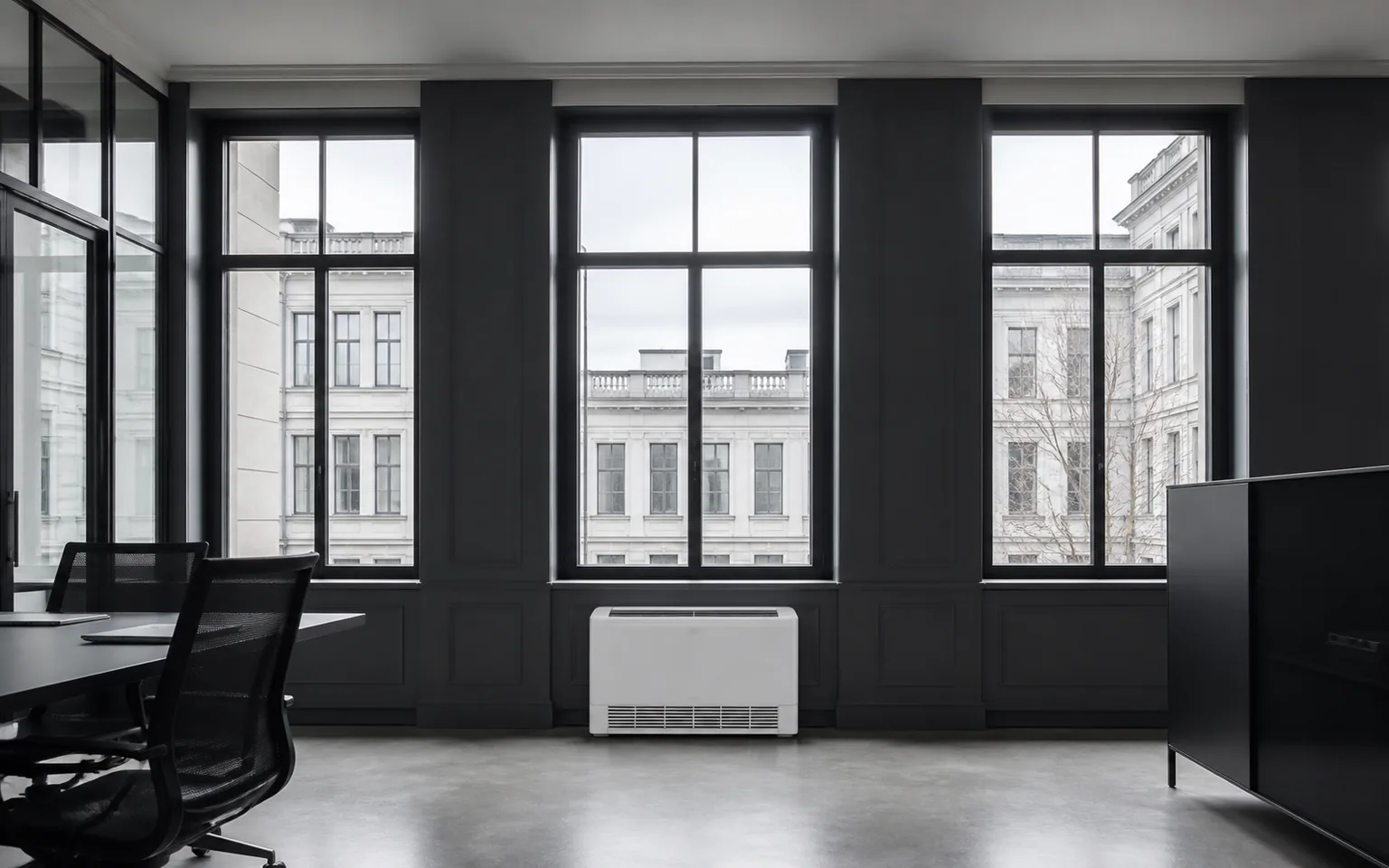Floor-standing air conditioning unit beneath tall windows in a protected commercial office